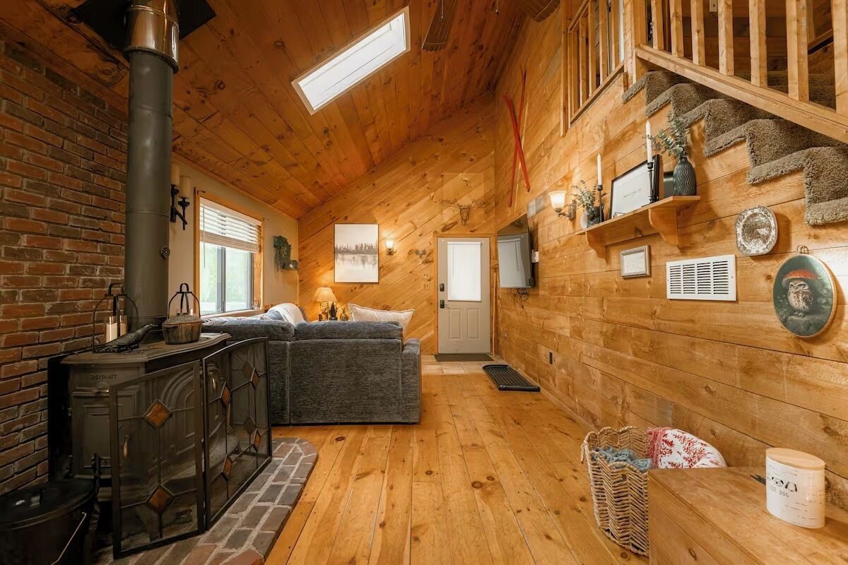 A cozy cabin interior with a fireplace, a sofa, and a staircase.