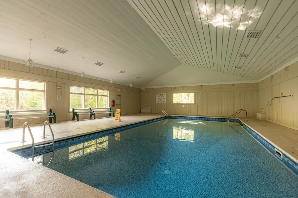 An indoor swimming pool with clear windows, a wooden ceiling, and a bench area.