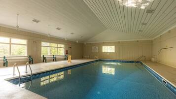 An indoor swimming pool with clear windows, a wooden ceiling, and a bench area.