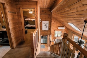 Innenansicht einer Holzhütte mit Treppe, Etagenbetten, einer Küchenzeile und einem Bild von einem Hirsch.