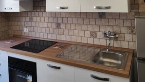 A kitchen with white cabinets, a stainless steel sink, a black stove, and a tiled backsplash.
