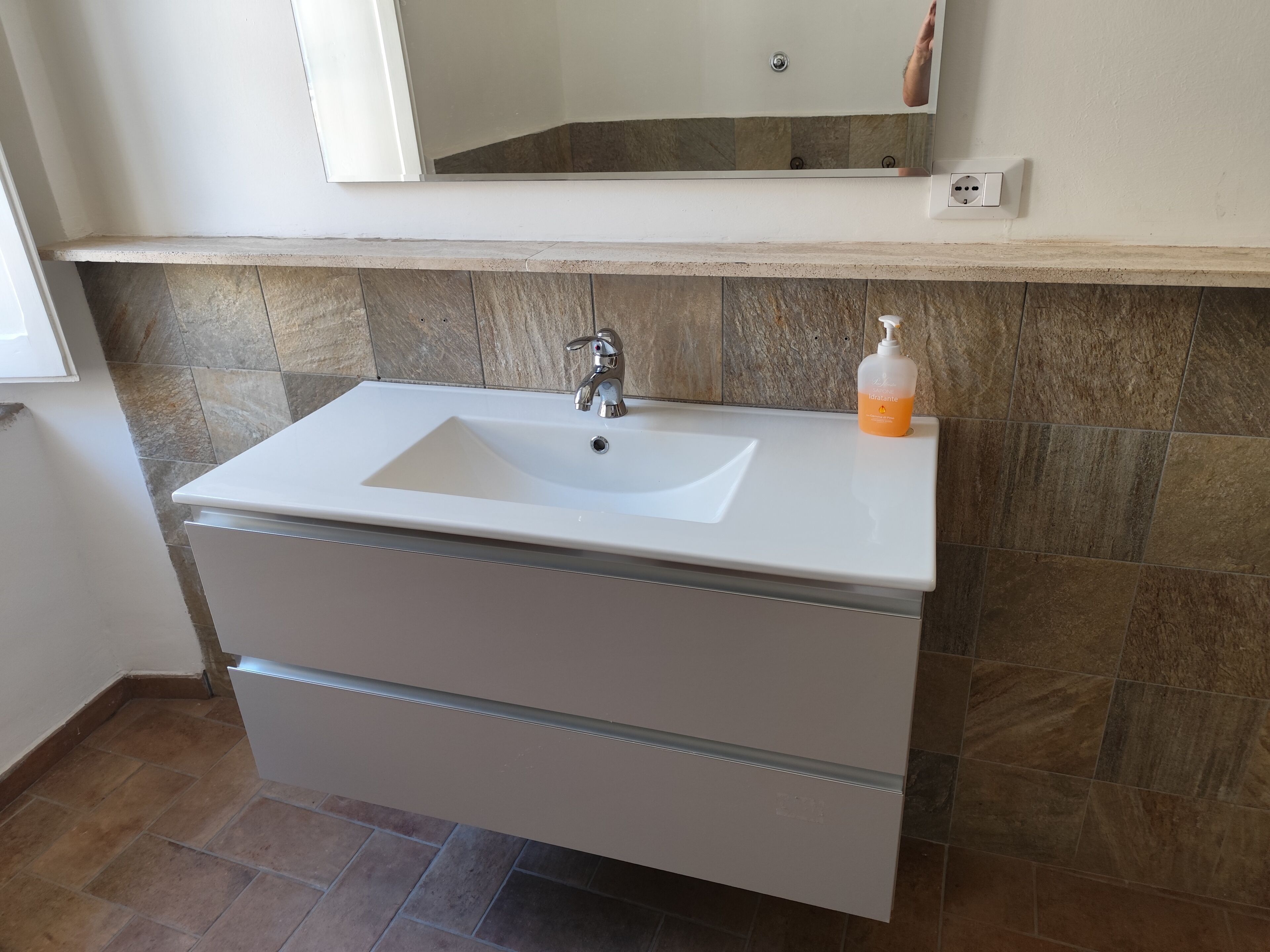 Une salle de bain avec un lavabo blanc, un miroir au-dessus et un flacon de savon posé sur le comptoir.