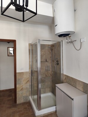 A shower enclosure with a glass door, a white cabinet, and a wall-mounted water heater. - Yos 1 Apartment (Vallerano)