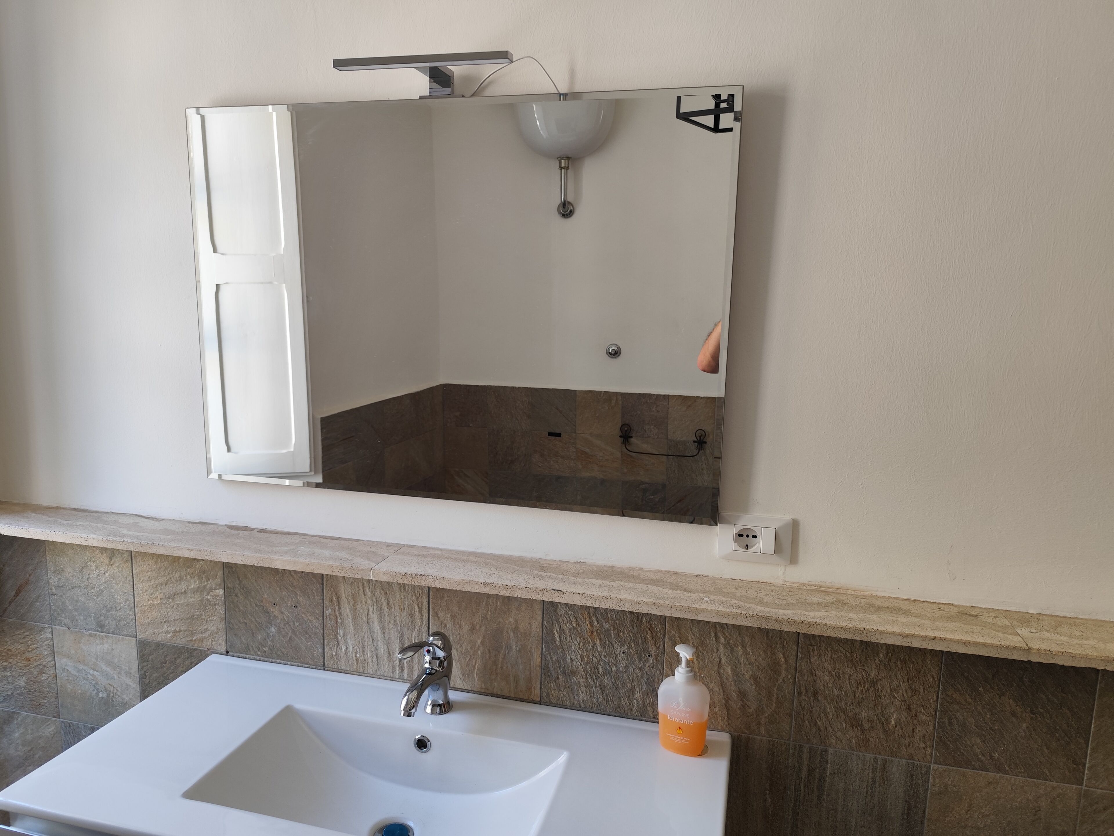 A bathroom with a white sink, a mirror with an open cabinet, and a shower area.