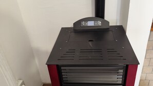 A wood stove with a digital control panel, a glass door, and a red frame.