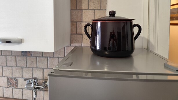 A stainless steel pot on a kitchen counter with a tiled backsplash and a white wall.