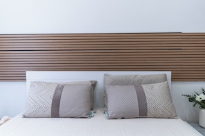Ein Bett mit zwei Kissen, einem Holz-Kopfteil und einer Vase mit Blumen.
