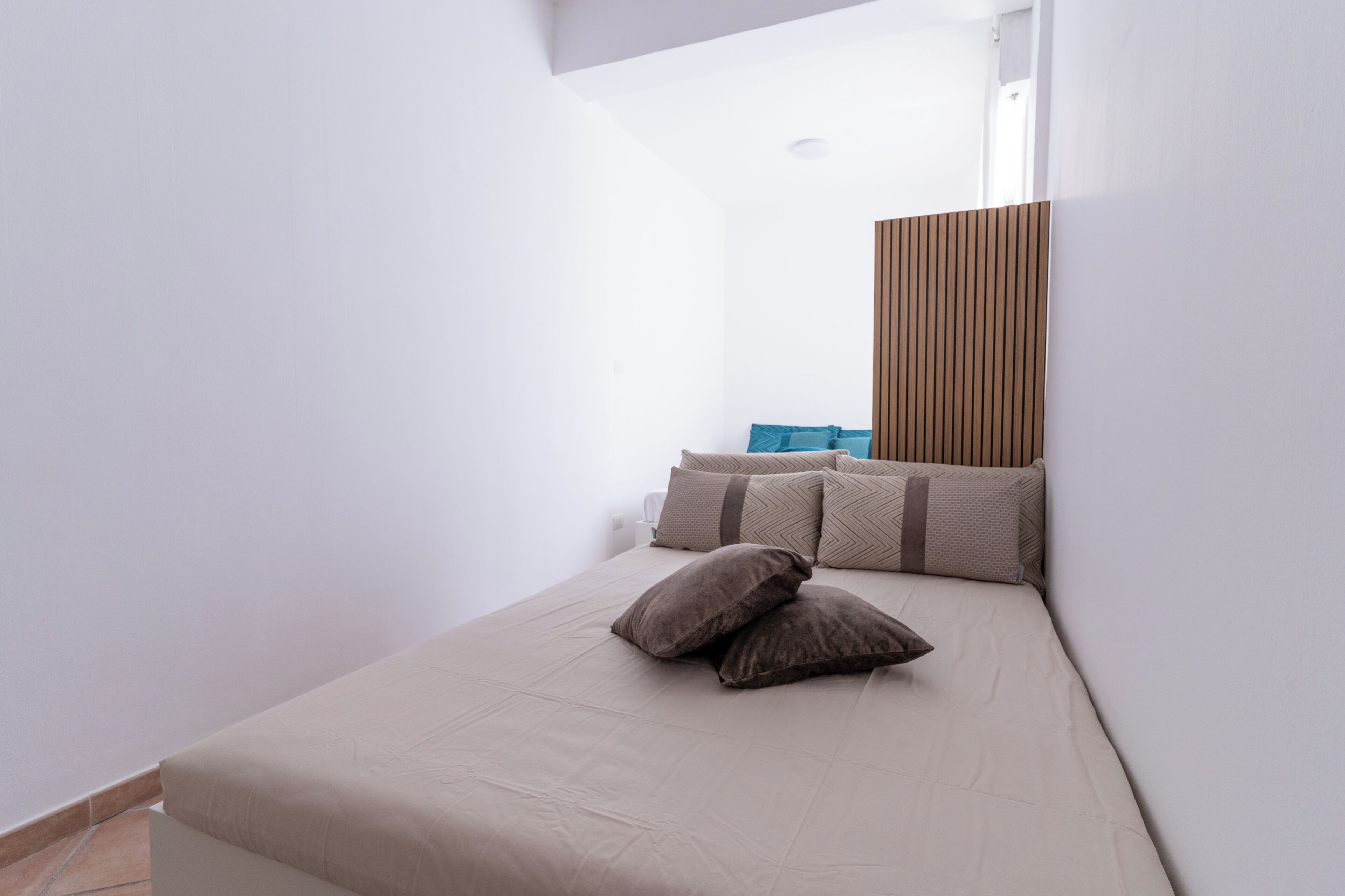 A small, modern bedroom with a bed, pillows, and a wooden headboard.