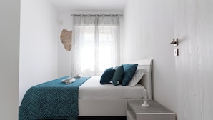 A modern bedroom with a bed, bedside table, and a window with sheer curtains.