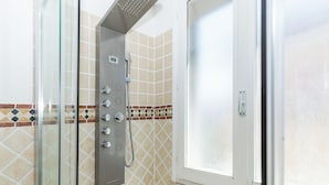 A shower with a glass enclosure, a control panel, and a tiled wall with a geometric pattern.