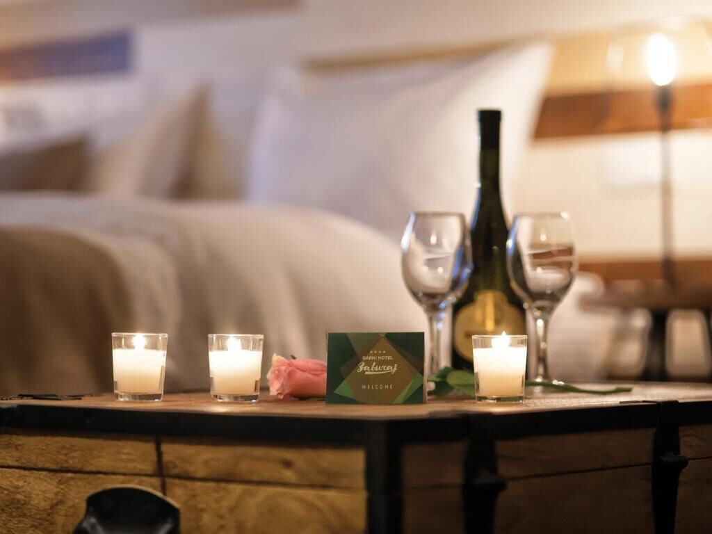 Une chambre d’hôtel avec un lit, une table de chevet avec des bougies, une bouteille et une carte de bienvenue.