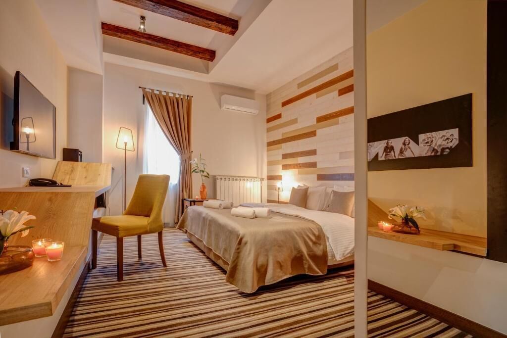 A hotel room with a bed, a desk, a chair, a bedside table with a vase of flowers, and a wall with artwork.