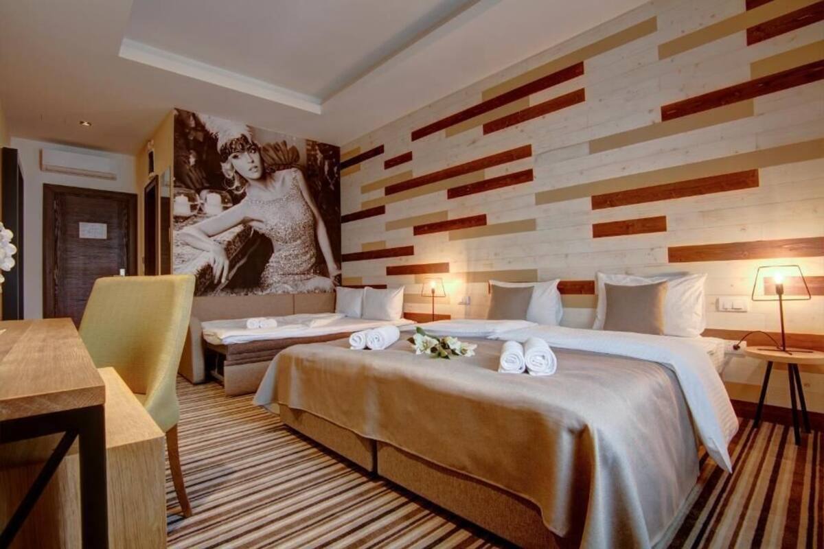 Habitación de hotel con dos camas, un mural grande en la pared y una zona de comedor con mesa y sillas.