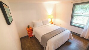 Ein Schlafzimmer mit Bett, Nachttisch, Lampe und Fenster.