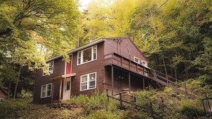 Ein zweistöckiges Holzhaus mit Veranda, umgeben von dichtem Wald.