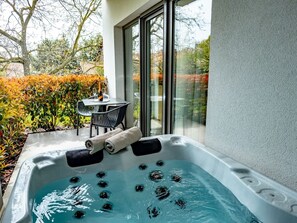 A hot tub with water jets, a table with chairs, and a glass door leading to a garden. - Premium apartment in the center of Tihany, with an outdoor hot tub and infrared sauna. (Tihany)