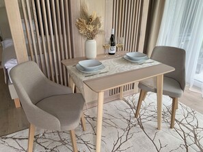 A dining area with a table, two chairs, a vase with dried flowers, and a bottle of wine. - Premium apartment in the center of Tihany, with an outdoor hot tub and infrared sauna. (Tihany)