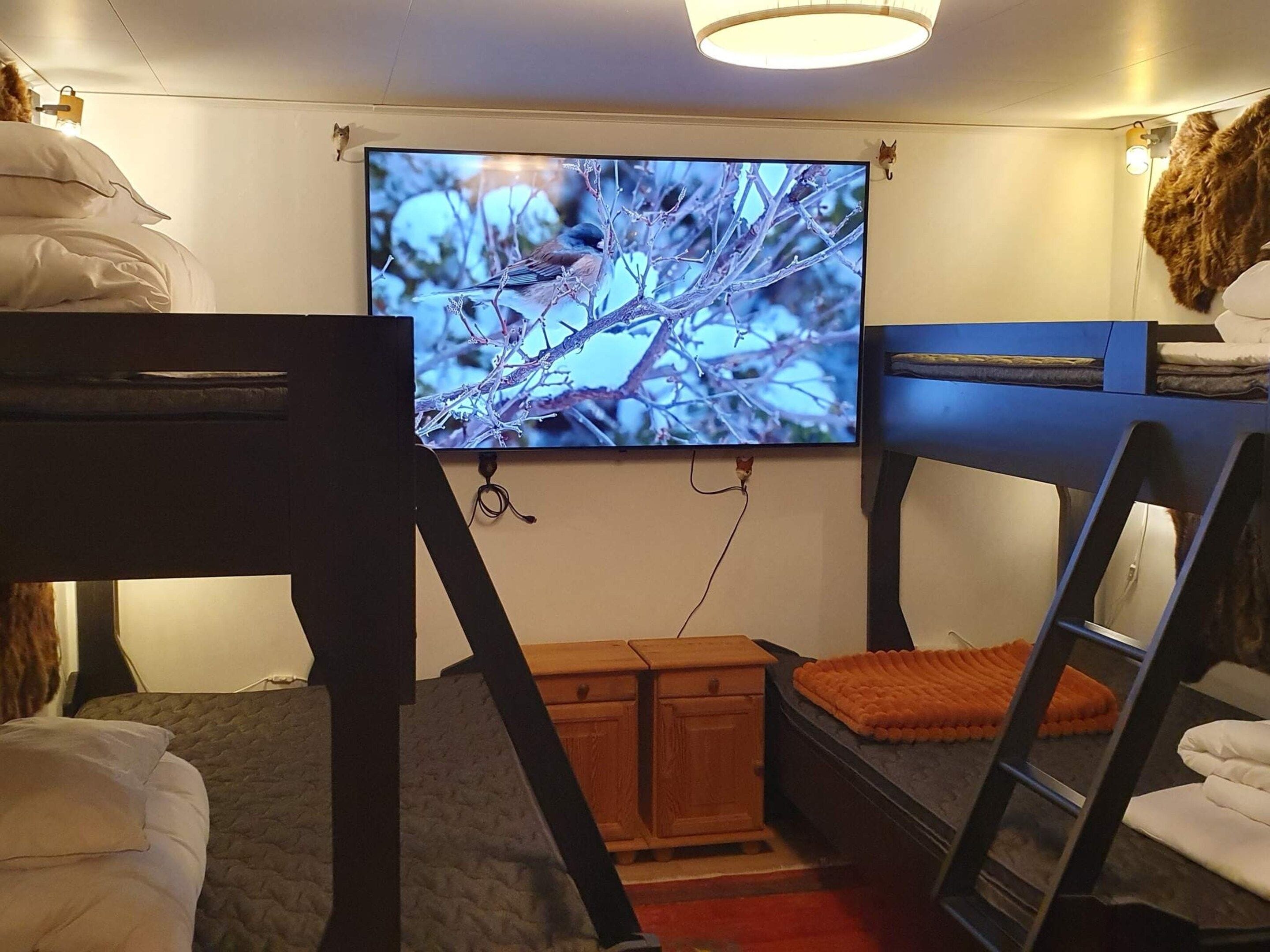A compact room with bunk beds, a television mounted on the wall, and a small wooden cabinet.