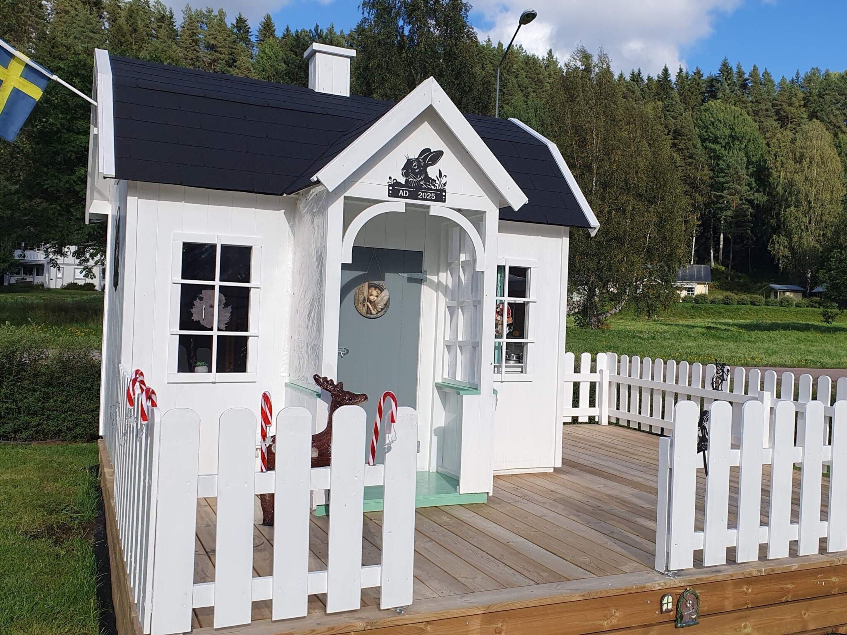 A white wooden house with a black roof, a white picket fence, and a mailbox.