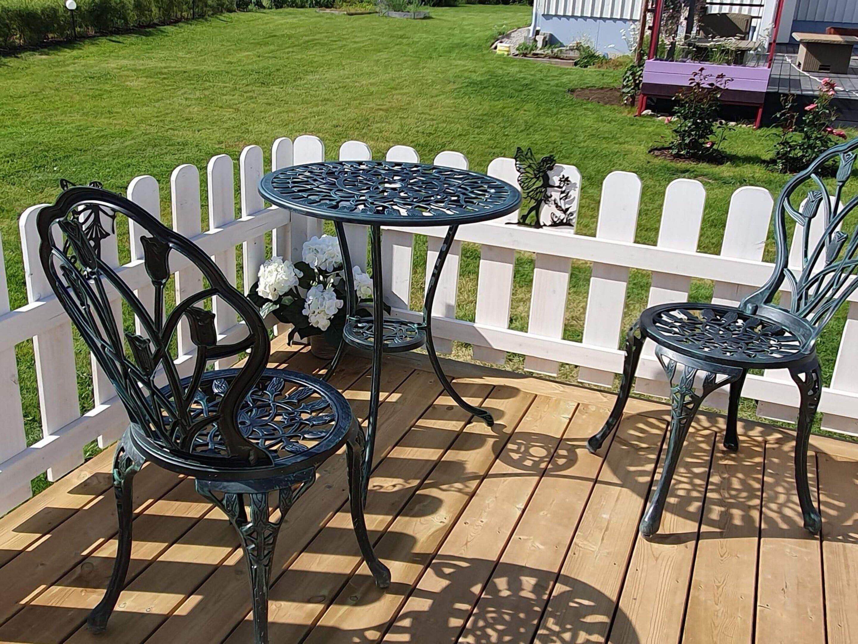 A wooden deck with a white picket fence, a round table, and two chairs.