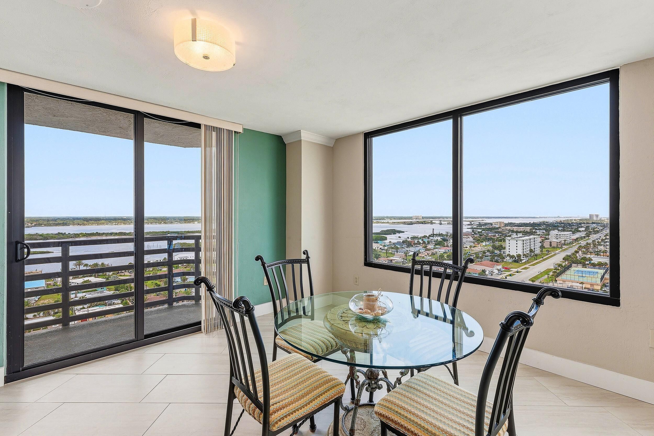 A balcony with a glass table and chairs, a view of a cityscape, and a door leading to a terrace.