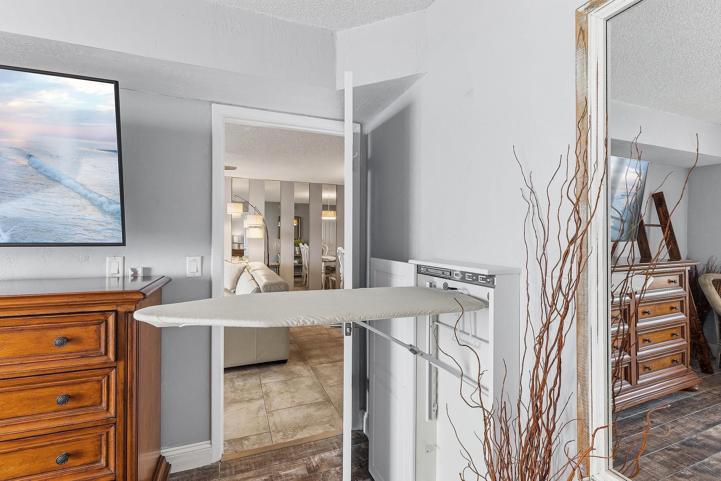 Ein Zimmer mit einem Holzkleiderschrank, einem Bügelbrett, einem Heizkörper und Blick auf einen Essbereich.