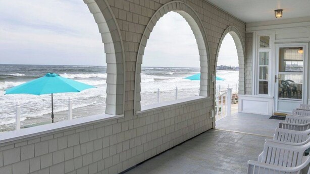 Un patio cubierto con paredes de ladrillo blanco y amplias ventanas arqueadas con vistas al océano.