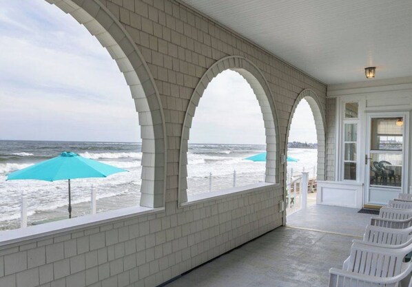 Eine überdachte Terrasse mit weißen Backsteinwänden und großen Bogenfenstern mit Blick auf den Ozean.