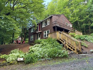 Eine zweistöckige Holzhütte mit einer Holzterrasse und einer Treppe, die zu einem Balkon führt.