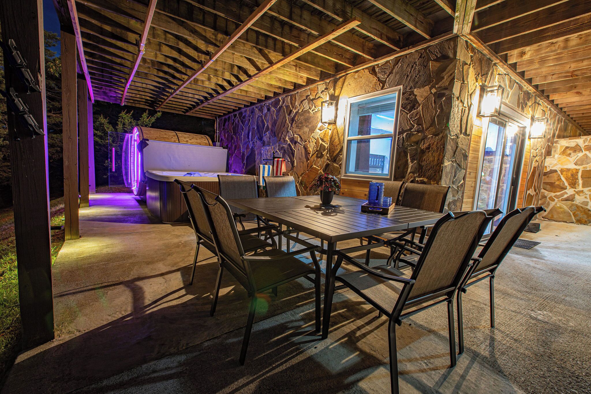 An outdoor dining area with a stone wall, wooden ceiling, and a view of the mountains.