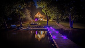 A lakeside cabin with a dock, surrounded by trees and a well-lit deck area.