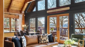 A cozy interior with a leather sofa, a dining area, and large windows offering views of the outdoors.