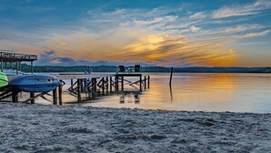 A beach with a wooden pier extending into calm waters, a covered seating area, and a row of boats.