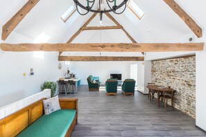 Un loft ampli amb sostre alçat, bigues de fusta a la vista, un sofà verd, una taula de dinar i una paret de pedra.