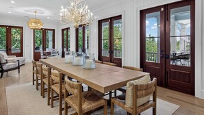 Un vaste espace dédié à la salle à manger, avec une longue table en bois, des chaises en osier et un lustre.