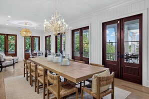 A spacious dining area with a long wooden table, wicker chairs, and a chandelier. - Ocean Views + Private Pool + Resort Amenities | 3301 Palm by Wild Dunes (Isle Of Palms)