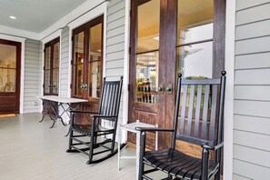 Eine Veranda mit zwei Schaukelstühlen und einem Tisch, Holztüren mit Glasfeldern sowie eine weiße Außenwand.