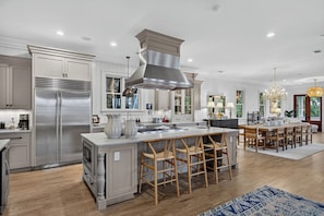 A modern kitchen with a central island, stainless steel appliances, and a dining area with wooden chairs. - Ocean Views + Private Pool + Resort Amenities | 3301 Palm by Wild Dunes (Isle Of Palms)
