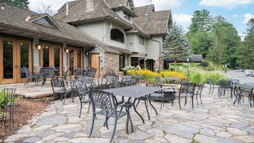 Une terrasse dallée de pierres, dotée de sièges extérieurs, et un bâtiment à la façade en pierre et aux nombreuses fenêtres.