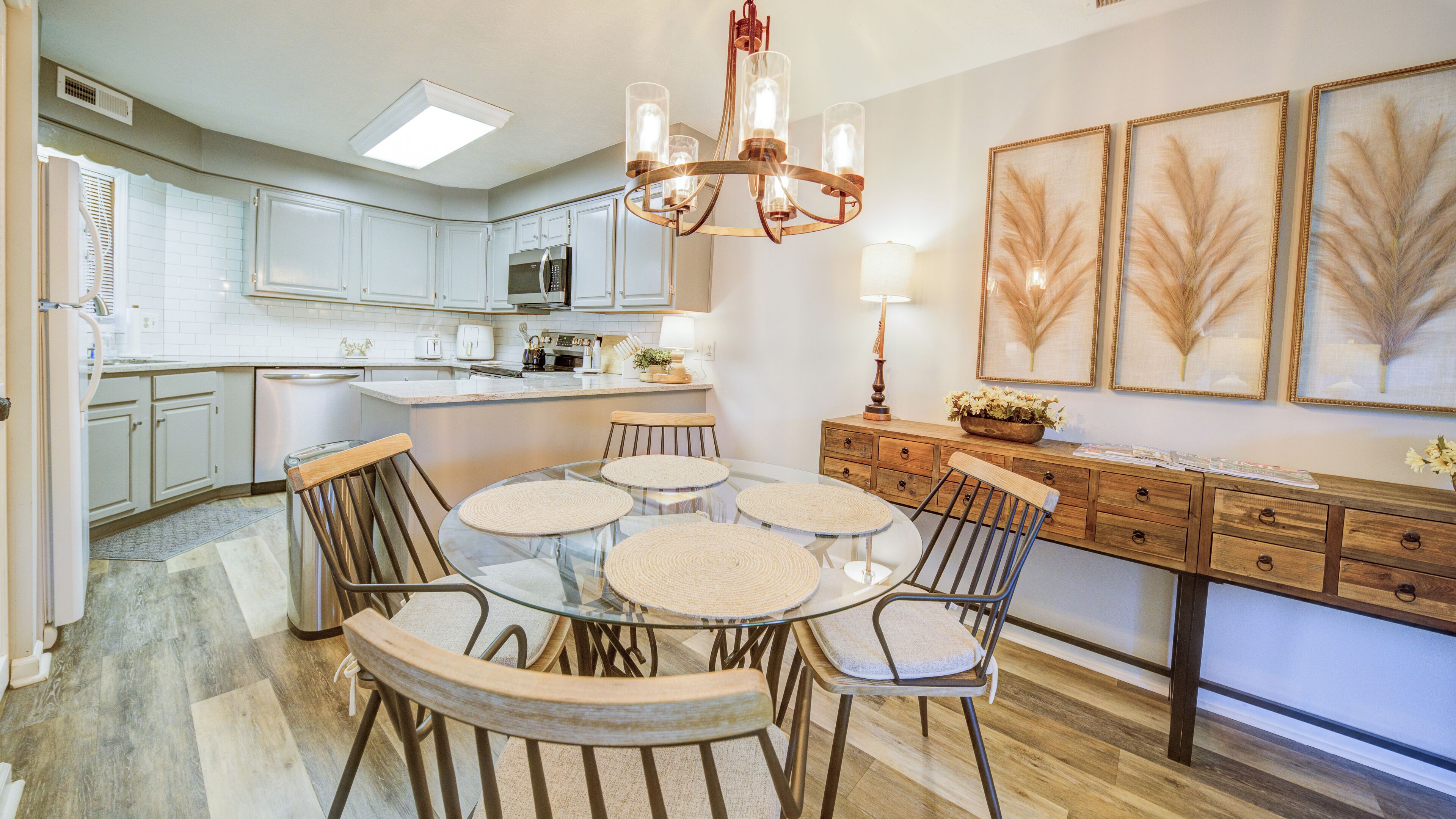 A modern kitchen with white cabinets, a central island, and a dining area with round tables and chairs.