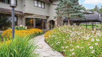 A two-story house with a stone facade, a stone pathway, and a garden with yellow and white flowers.