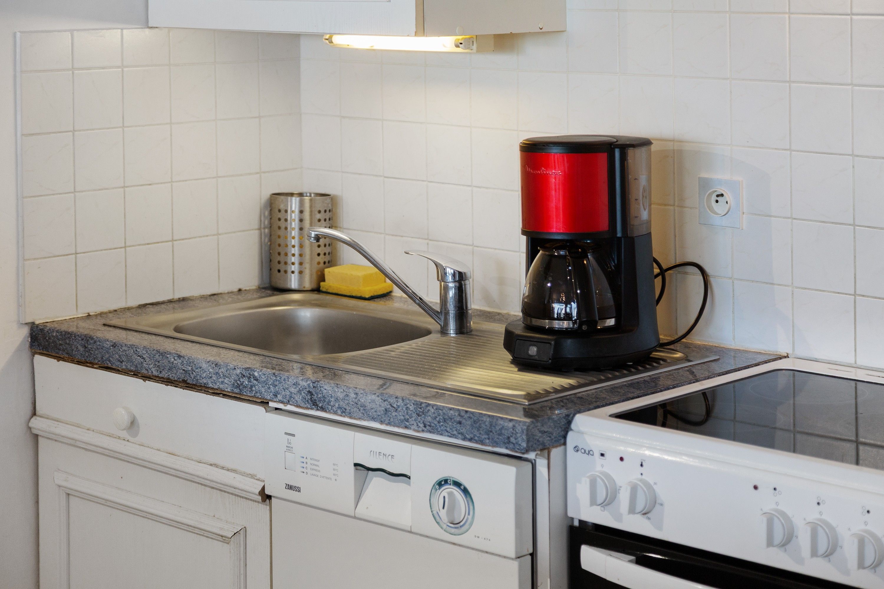 Une cuisine équipée d’un évier à deux bacs, d’une machine à café, d’une râpe et d’un lave-vaisselle.