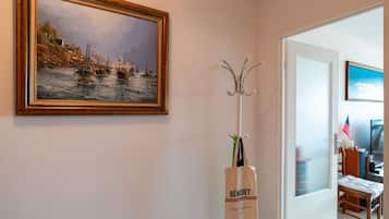 Un couloir avec un tableau encadré représentant des bateaux, un porte-manteau, une porte blanche et une chaise.