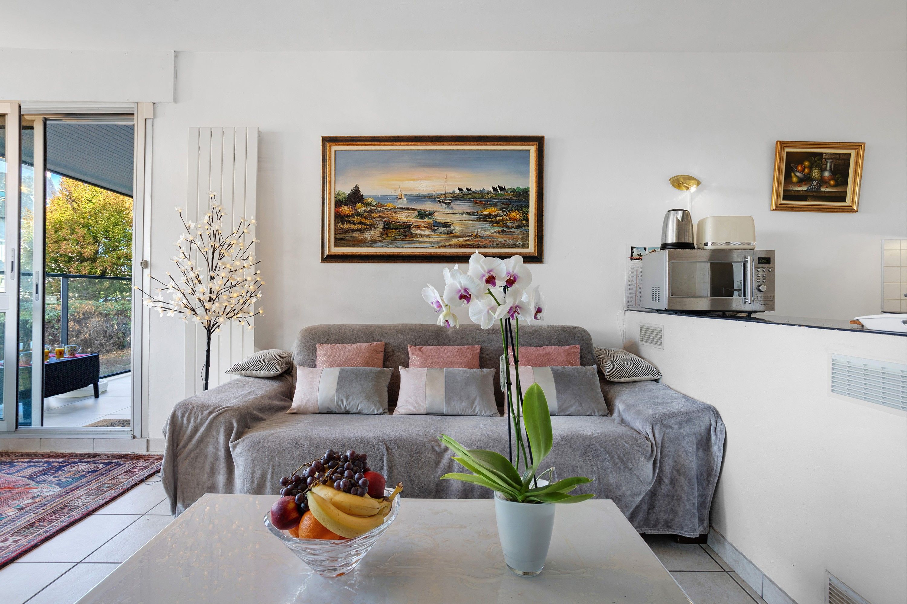 Un salon avec un canapé, un tableau, un panier de fruits et une plante en pot.