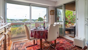 Comedor con mesa lista para cuatro personas, ventanas amplias y vistas a zonas verdes y edificios.