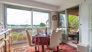 Un coin repas avec une table dressée pour quatre personnes, de grandes fenêtres et une vue sur la verdure et les bâtiments.