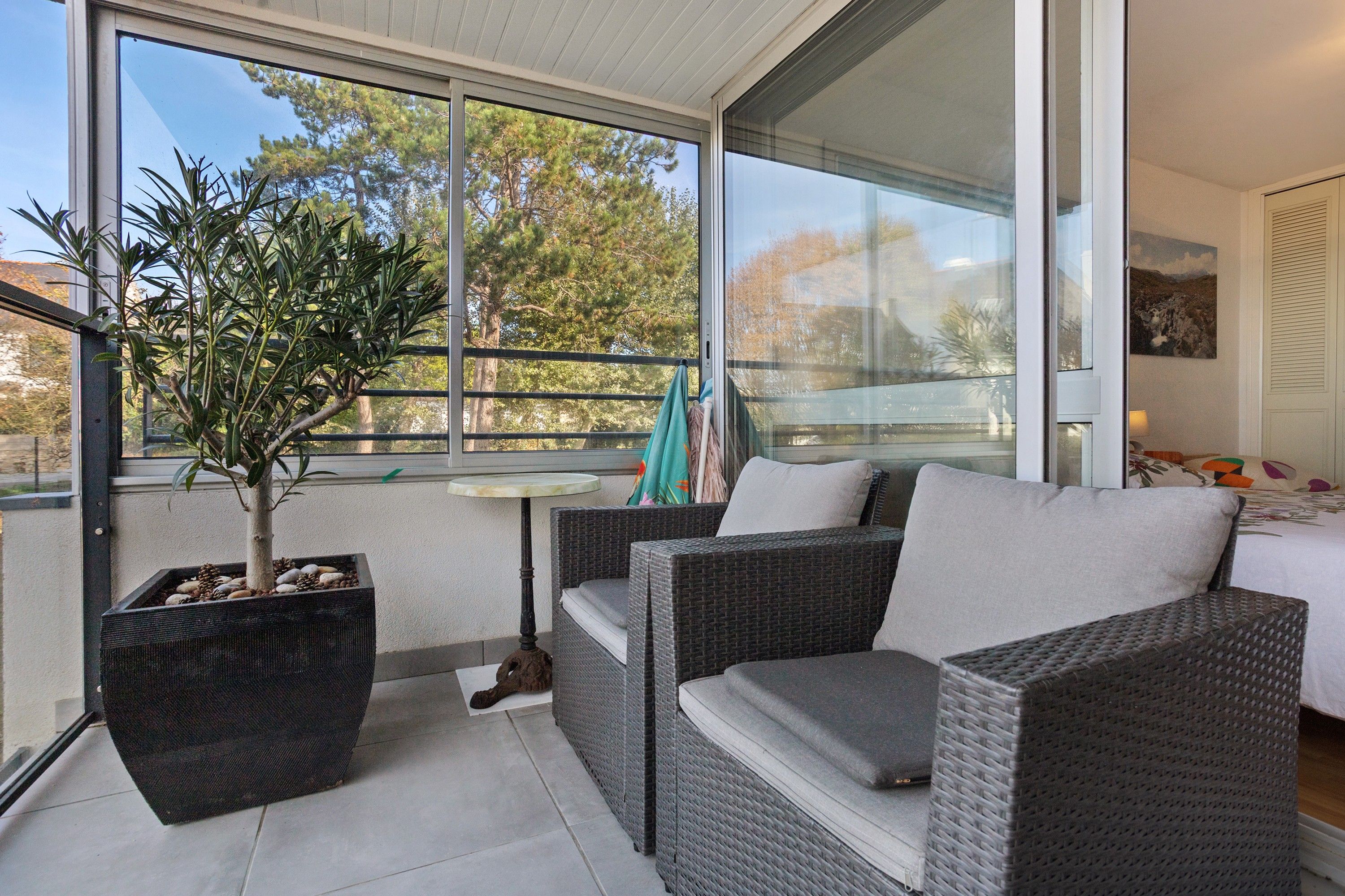A balcony with wicker furniture, a potted plant, and a view of trees.