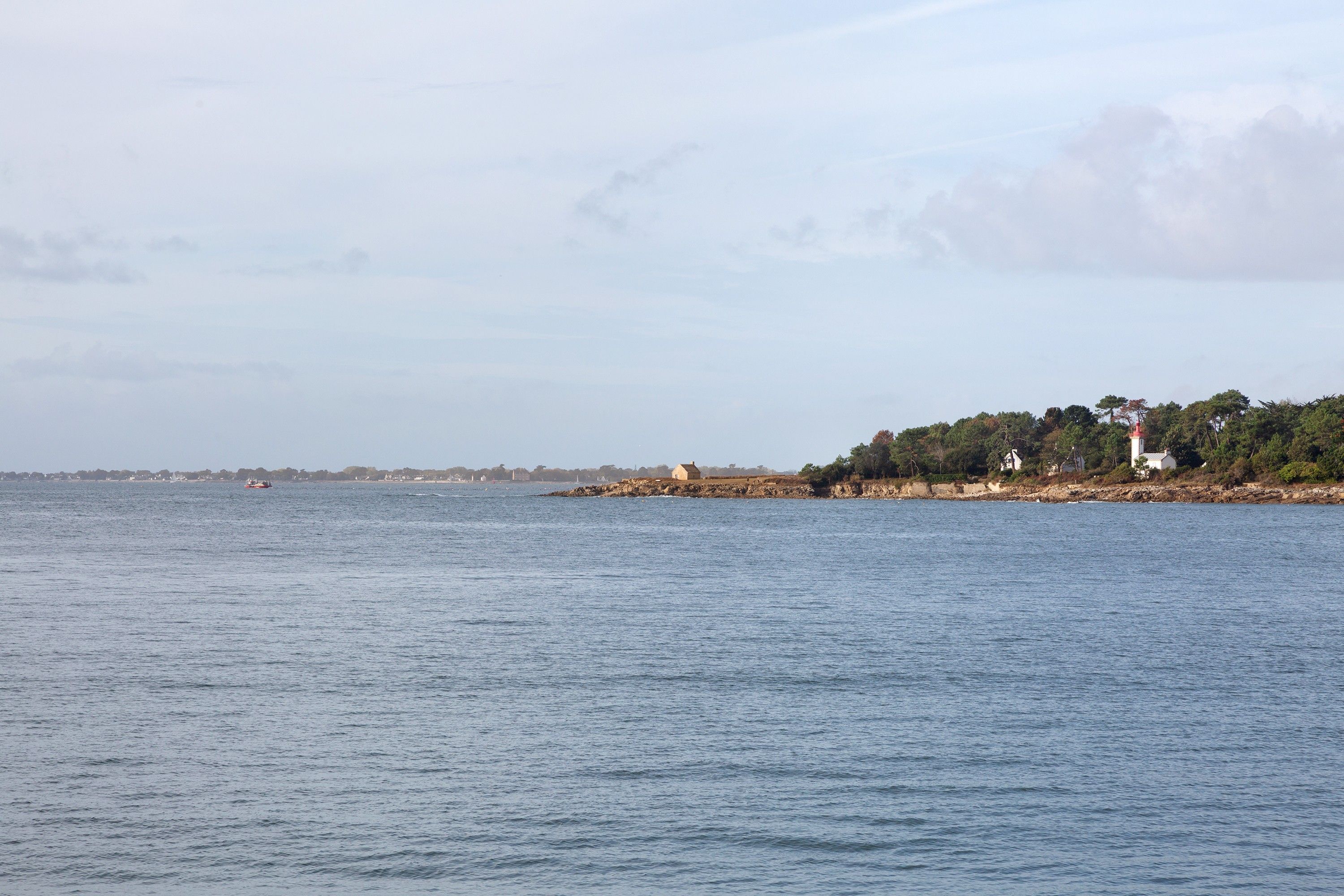 A coastal view with a lighthouse, calm sea, and distant shoreline.