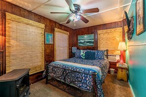 Ein Schlafzimmer mit Bett, Deckenventilator, Heizkörper und einem Fenster mit Jalousien.