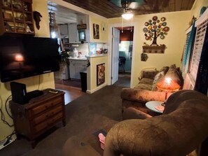 A living room with a television, a sofa, a wooden dresser, and a dining area in the background. - Whimsical Mermaid Retreat with Private Deck in Bacliff, Texas (Bacliff)